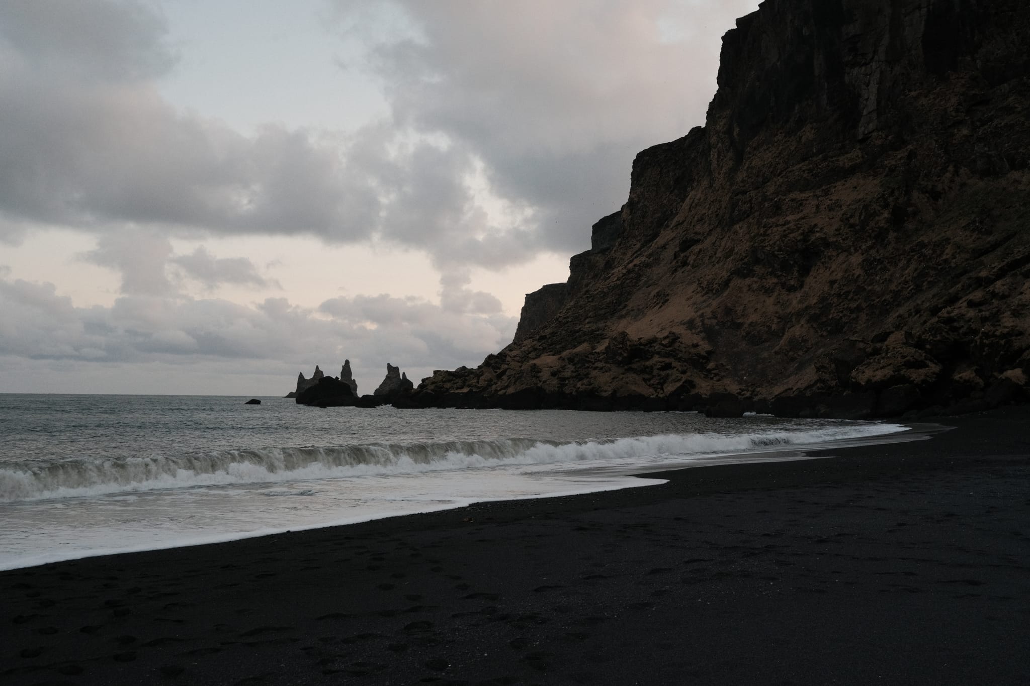 Black Sand Beach — Waves break on black sand below dark cliffs.