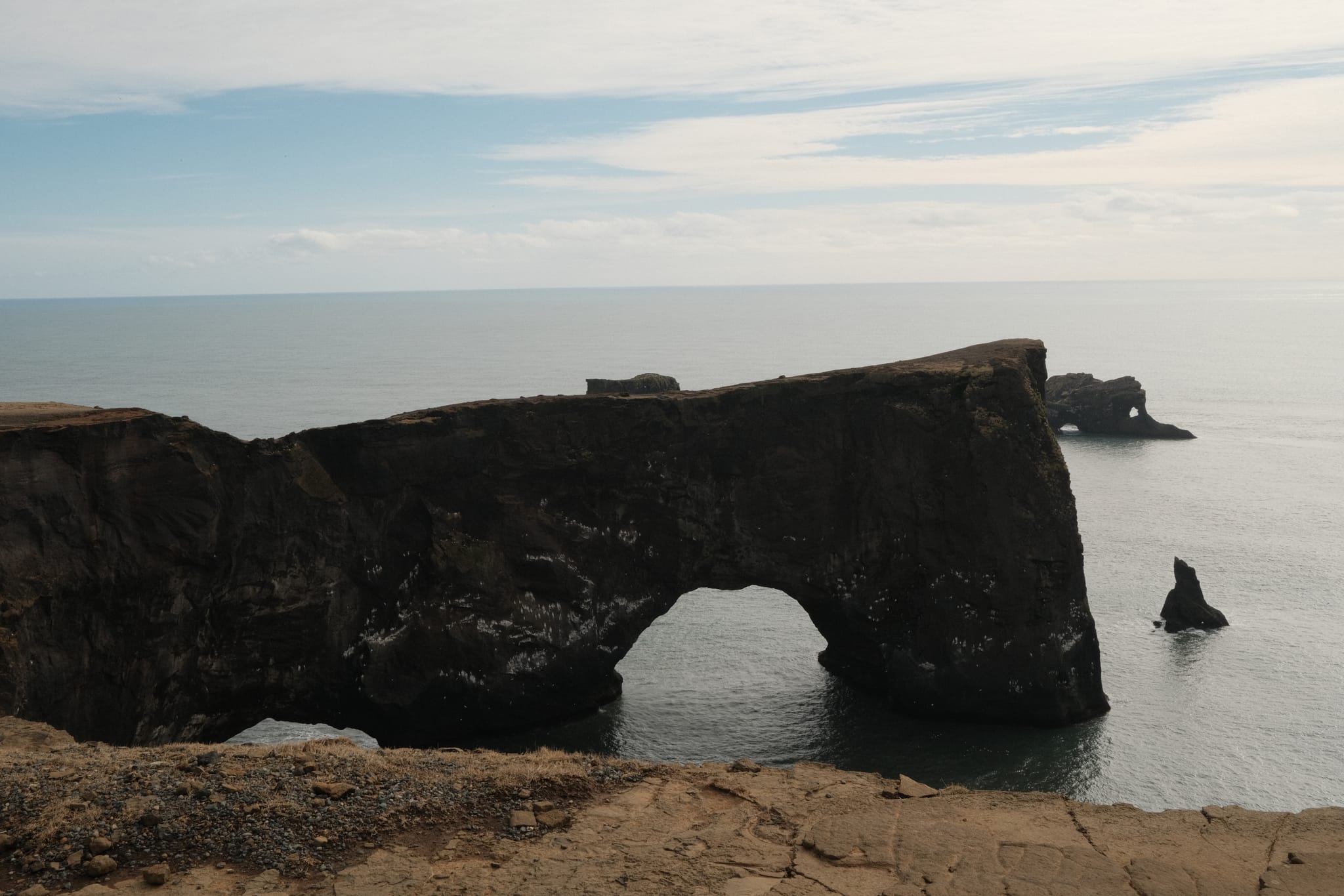 Dyrholaey Arch — A black stone arch reaches into the sea.