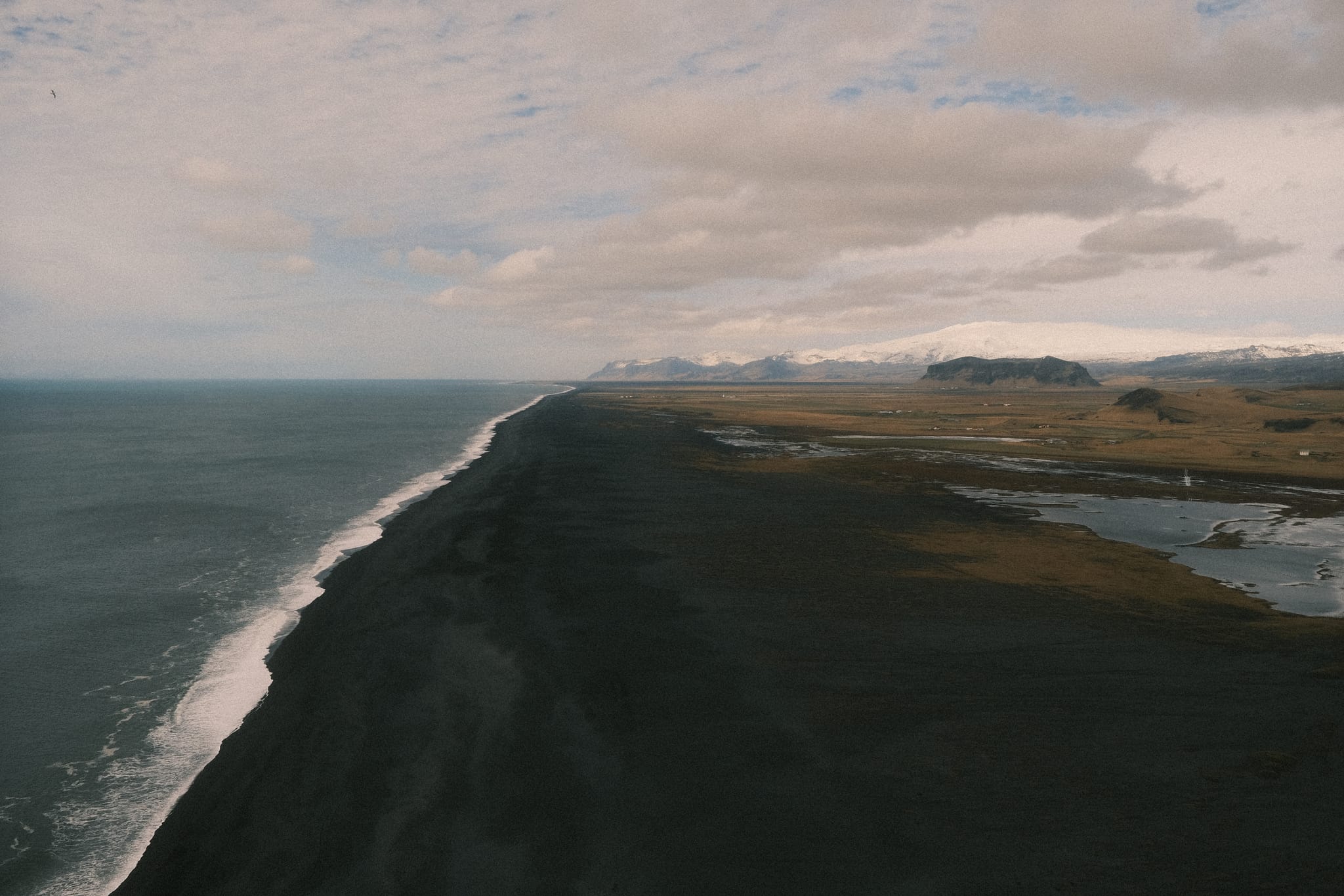 Endless Black Shore — Surf traces a black coast toward distant peaks.