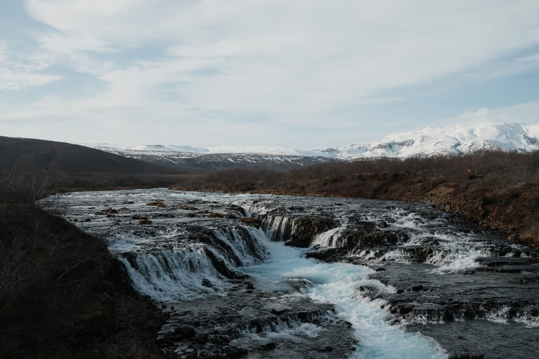 Blue River Falls — A turquoise river spills below snowy peaks.